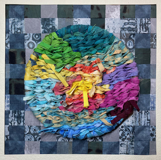 A circle woven from strips of fabric in colours of a rainbow. The background in a fabric patchwork in blues and greys.